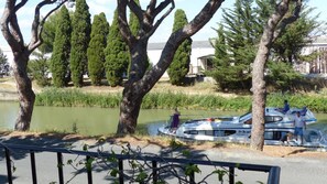 Une rivière avec un bateau amarré sur la rive droite, entourée d’arbres et avec un bâtiment visible au loin.