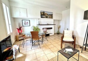 A living room with a glass-top dining table, two chairs, a sofa, a television, and a fireplace.