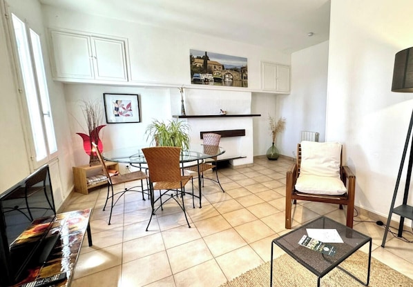 A living room with a glass-top dining table, two chairs, a sofa, a television, and a fireplace.