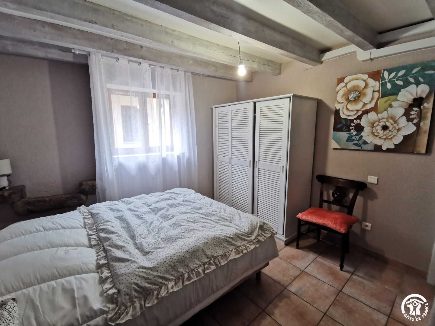 A bedroom with a bed, a chair, a wardrobe, and a painting on the wall.