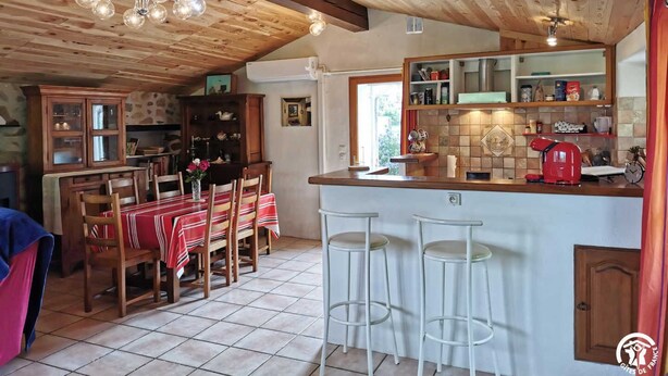 Eine gemütliche Küche mit Holzbalken, einem Essbereich mit rot-weiß kariertem Tischlein und einer Bar mit Barhocker.