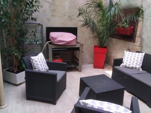 Un espace extérieur aménagé avec des meubles en osier, un pot de fleurs rouge et une plante en pot.
