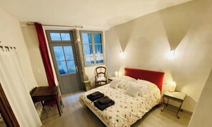 Une chambre à coucher avec un lit, une chaise, une table et une fenêtre avec des rideaux.