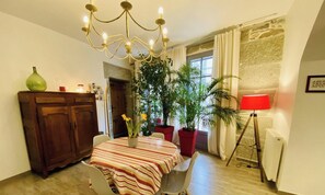 Un coin repas comprenant une table ronde, des chaises, un lustre, des plantes en pot, un meuble et un lampadaire rouge.
