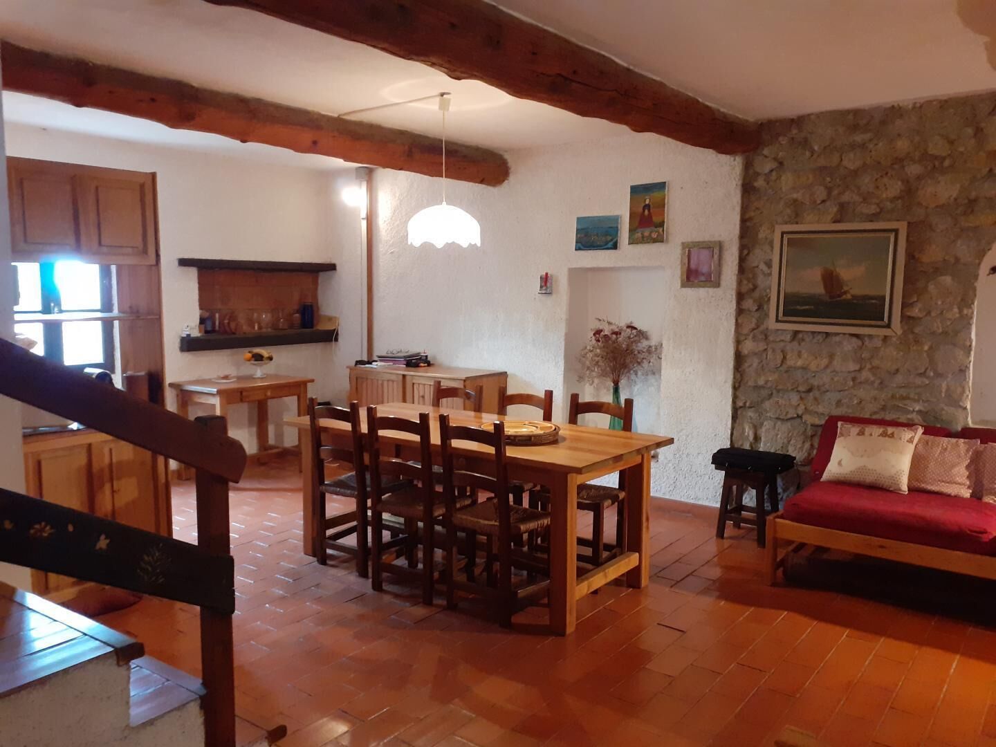A cozy living room with a wooden dining table and chairs, a red sofa, and a stone wall.
