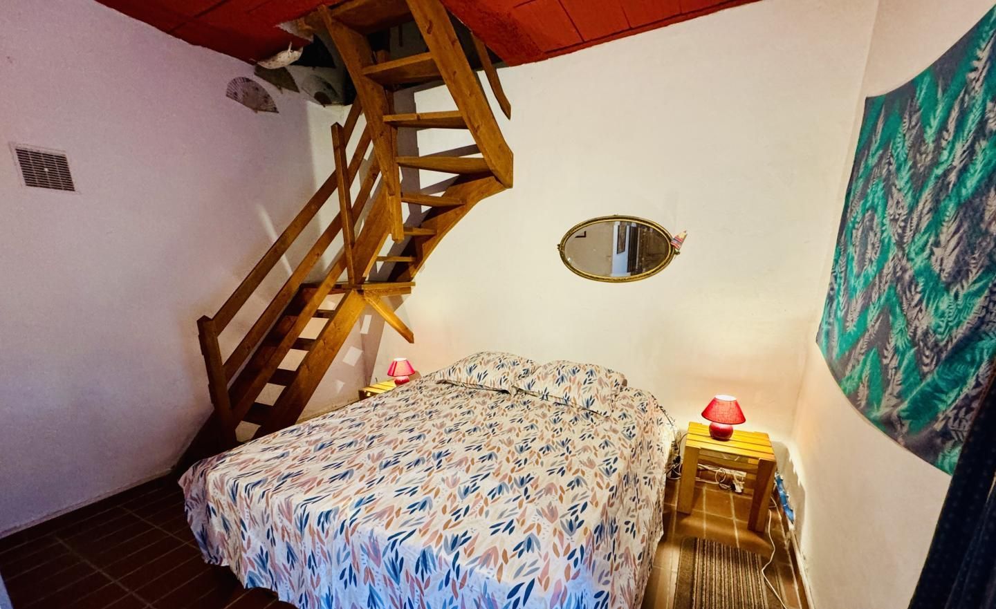 Un dormitorio con cama, una escalera de madera, una mesita con lámpara y un espejo en la pared.