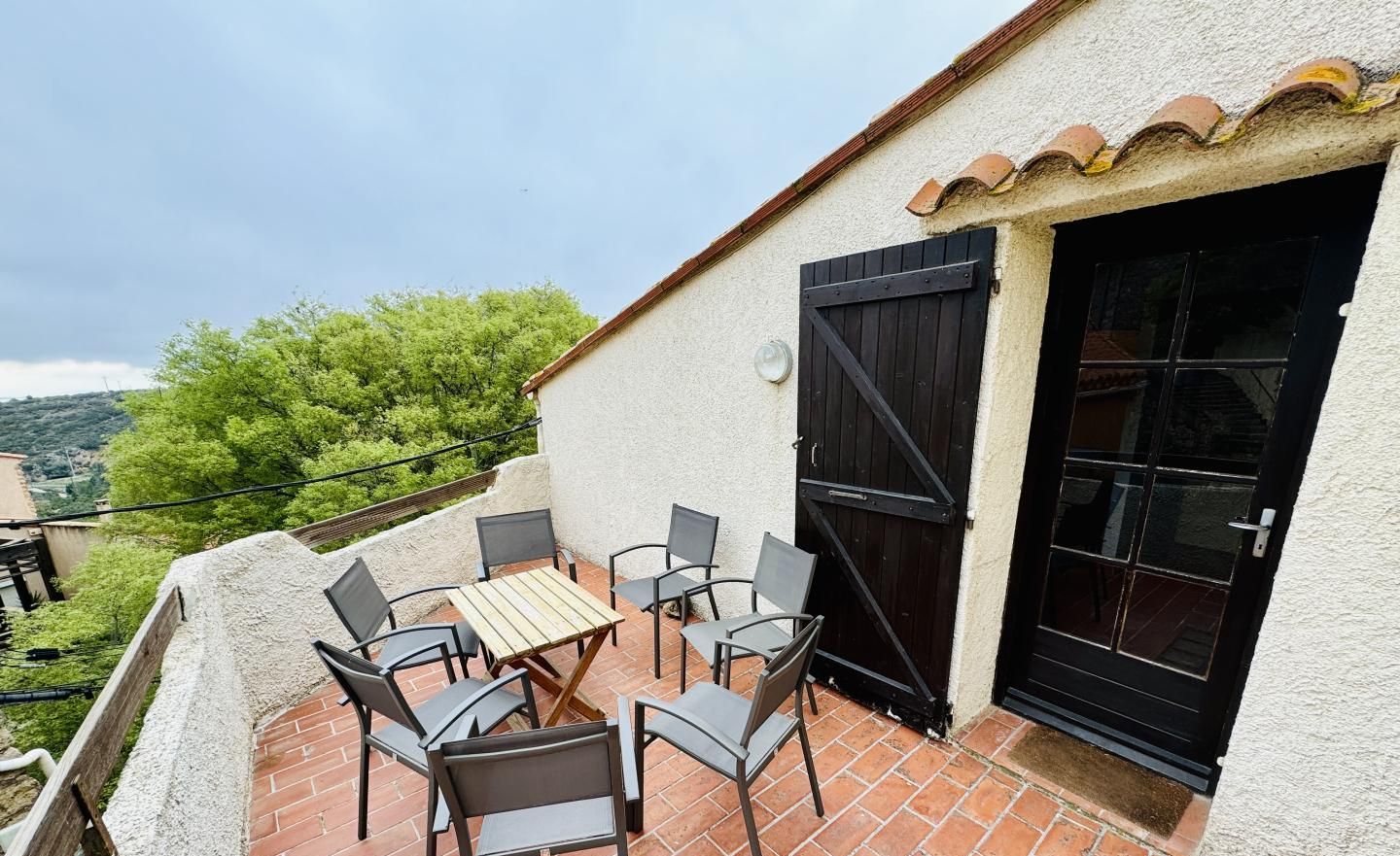 A terrace with a table and chairs, a black gate, and a view of greenery.