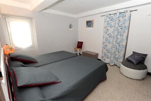 A room with two beds, a chair, a bench, a window with curtains, and a wall-mounted picture.