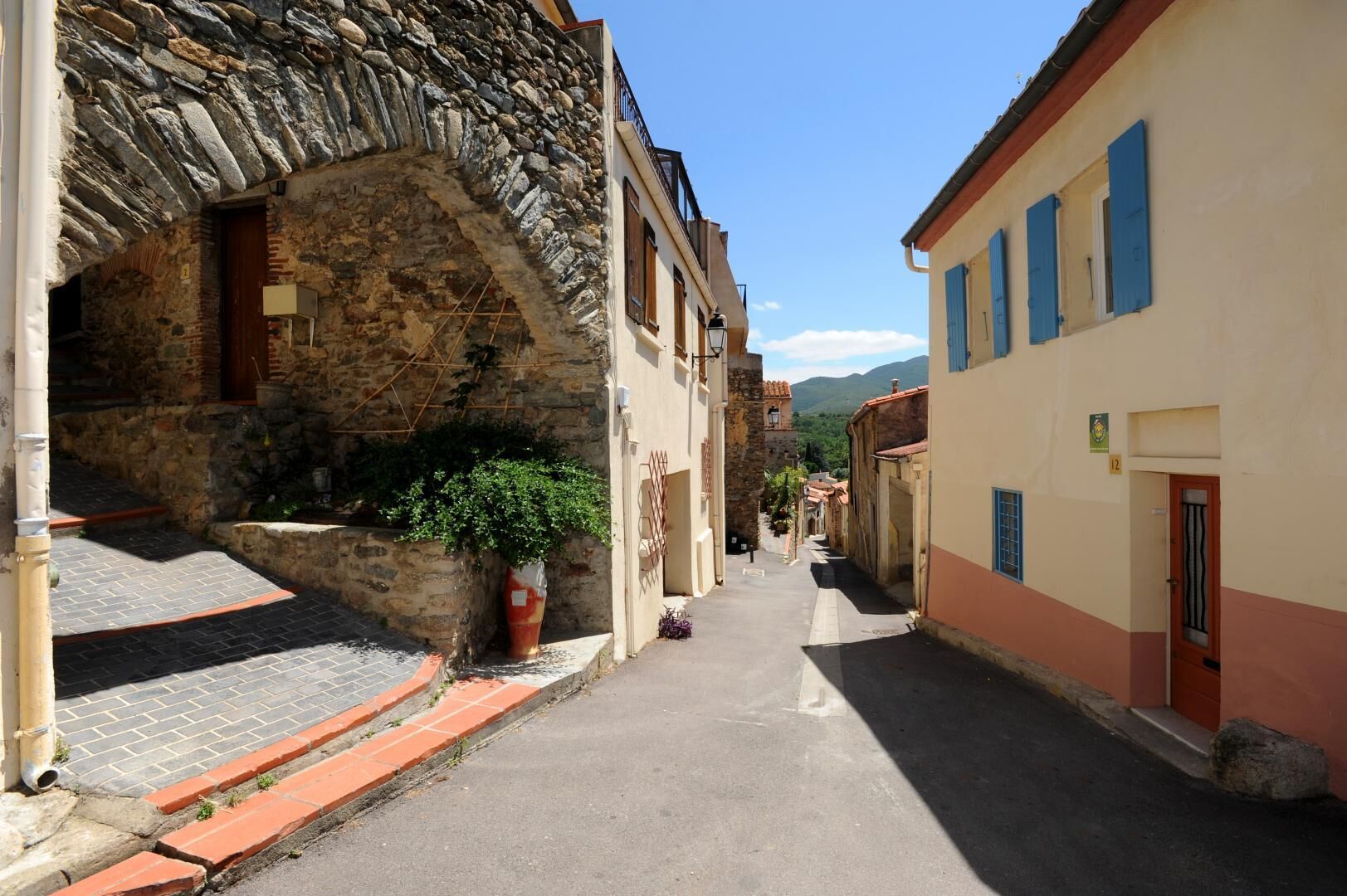 A narrow street with stone buildings, a potted plant, and a clear sky.