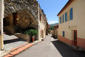 A narrow street with stone buildings, a potted plant, and a clear sky.