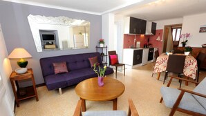 A modern living room with a sofa, a round wooden table, and a dining area with chairs and a table set for two.
