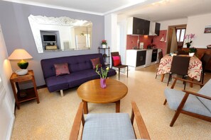 A modern living room with a sofa, a round wooden table, and a dining area with chairs and a table set for two.