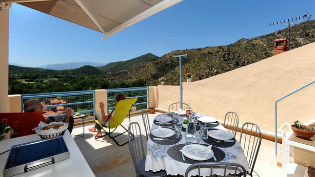 An outdoor dining area with a table set for four, overlooking a mountainous landscape.