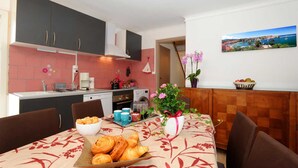 A compact kitchen with modern appliances, a dining area with a table set for two, and a view of a coastal town through a window.
