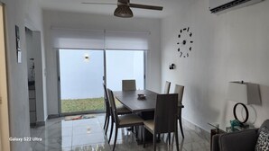 Un salon moderne comprenant un coin repas, un ventilateur de plafond, une horloge murale et une grande fenêtre donnant sur l’extérieur.