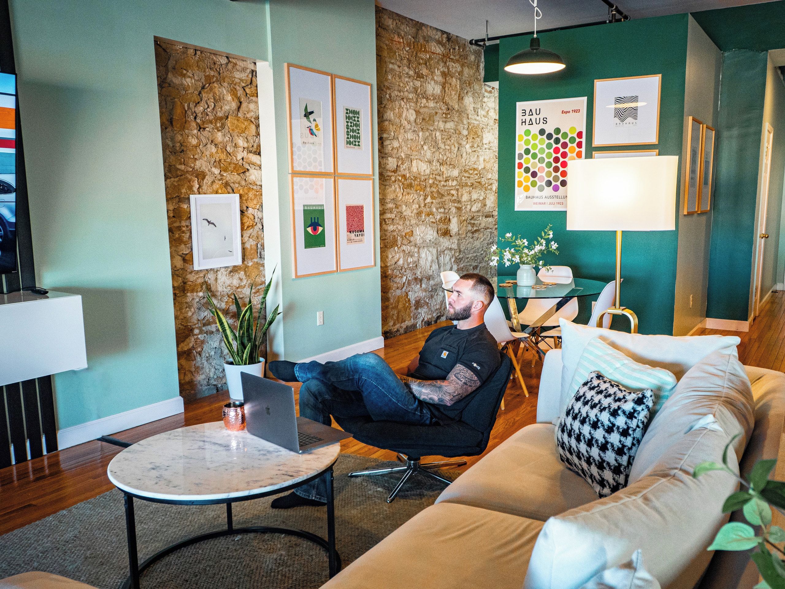 Een modern interieur met een stenen muur, een ronde tafel met een laptop, een bank en een lamp.