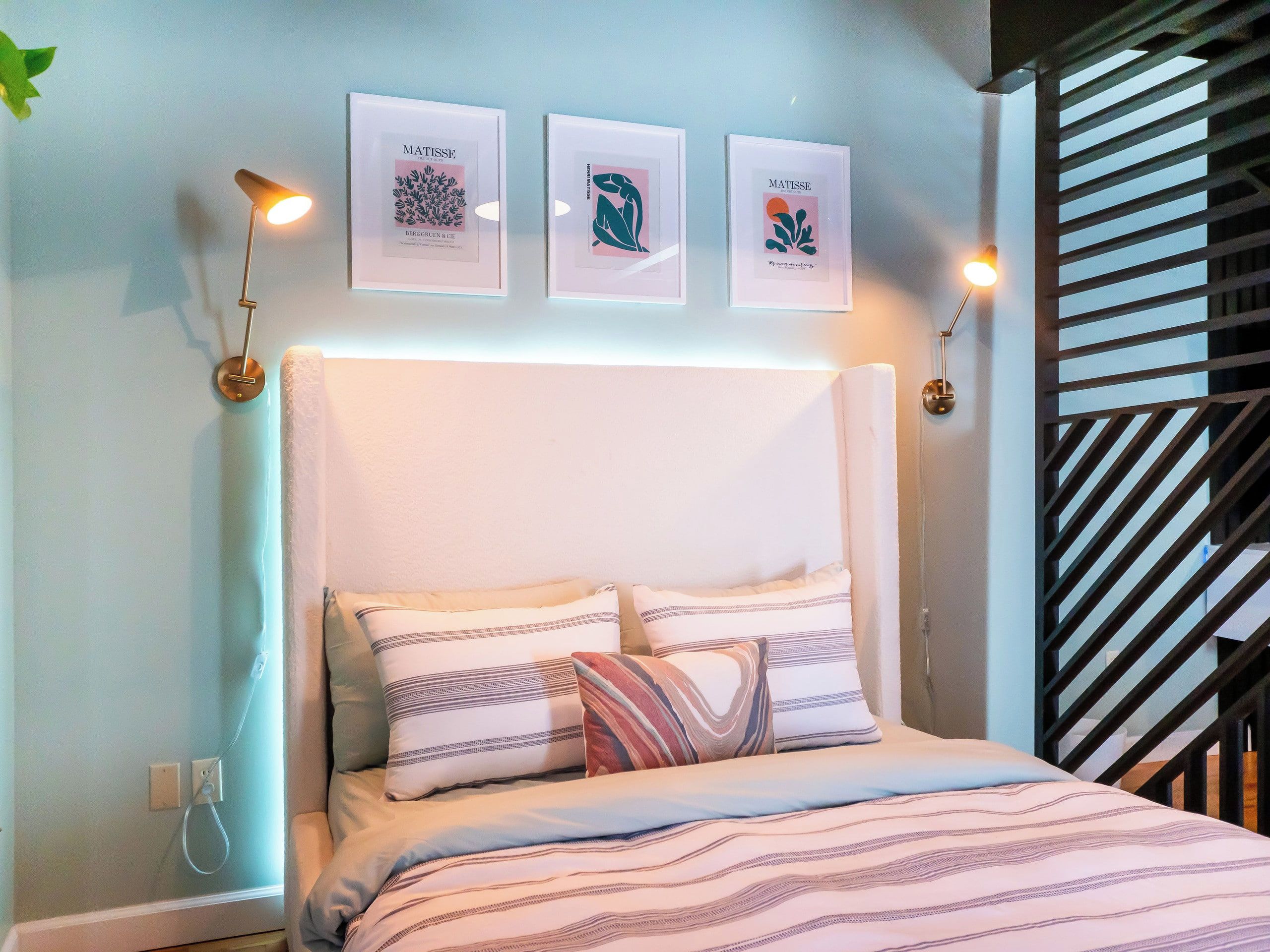 Ein Schlafzimmer mit einem Bett, Kissen, einem Kopfteil und drei gerahmten Kunstwerken an der Wand.