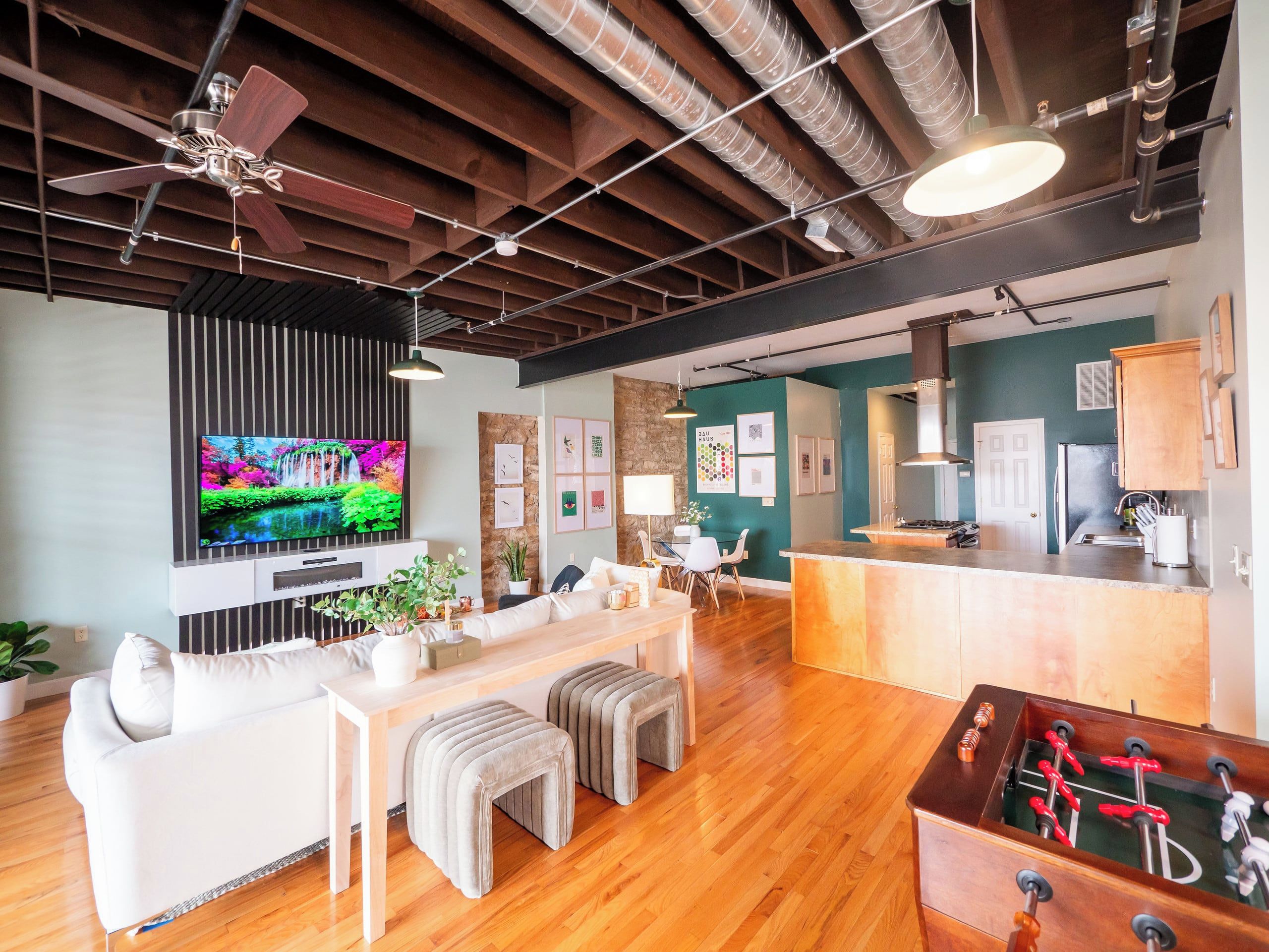 A modern living room with a TV, sofa, ottomans, and a foosball table.