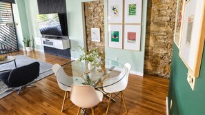 Ein modernes Wohnzimmer mit Glastisch, zwei Stühlen, einem Flachbildfernseher, einer Steinwand und gerahmten Kunstwerken.