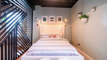 Une chambre moderne avec un lit, deux tabourets blancs, un escalier et des lampes fixées au mur.