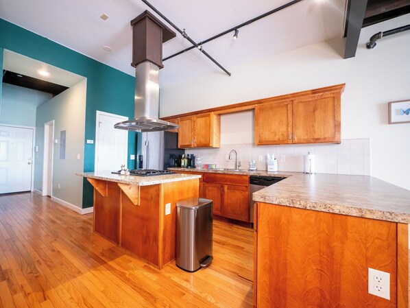 A modern kitchen with wooden cabinets, a stainless steel range hood, and a granite countertop.
