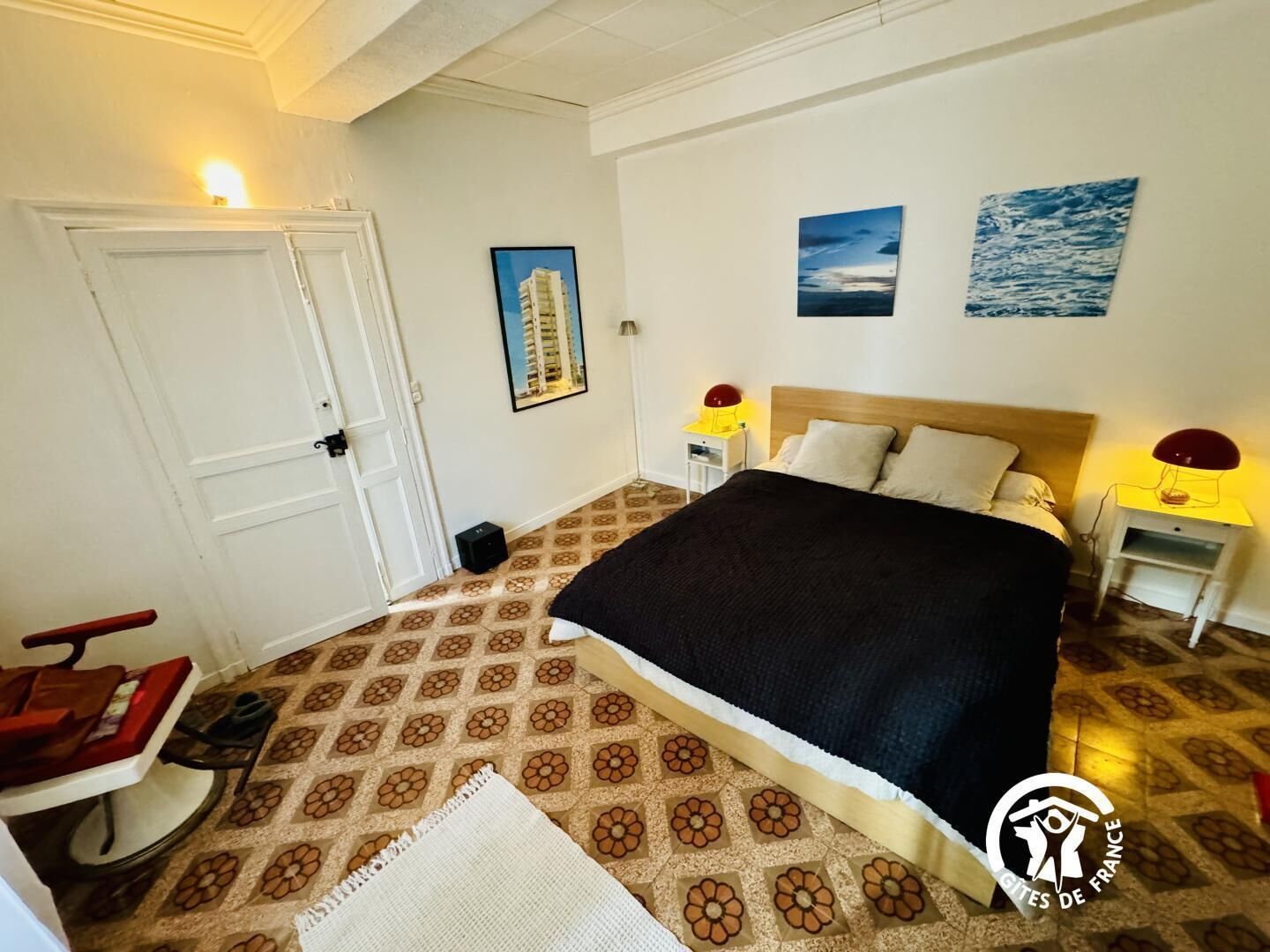 Une chambre d’hôtel avec un lit, deux tables de chevet avec des lampes, une chaise, une porte et un tapis à motifs.