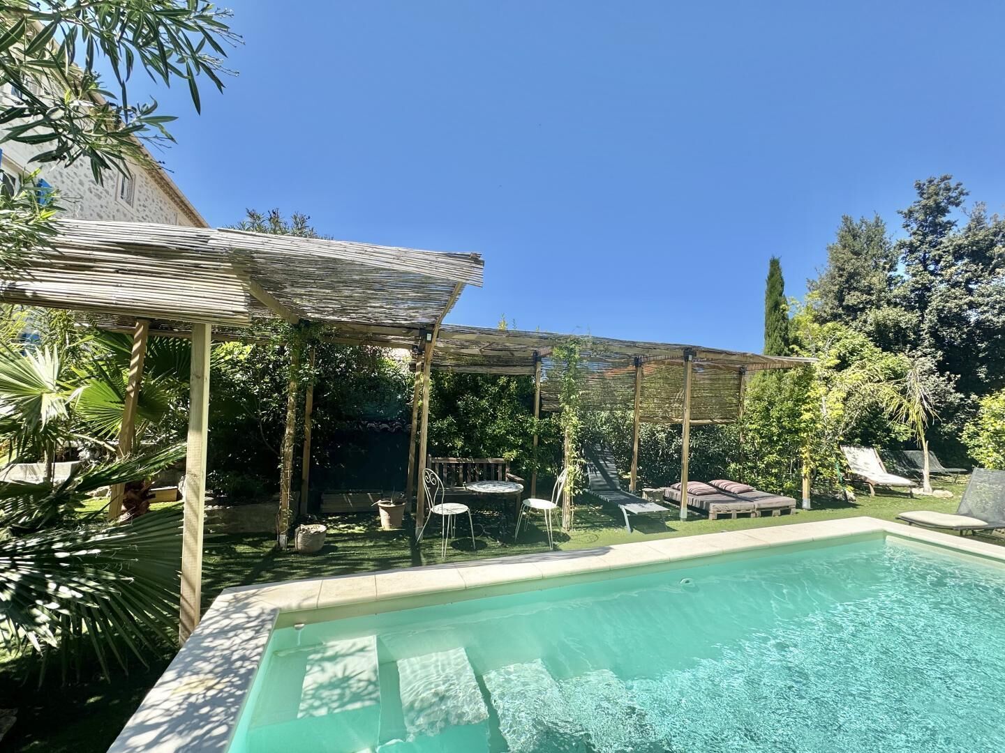 A swimming pool with a pergola and lounge chairs, surrounded by greenery and trees.