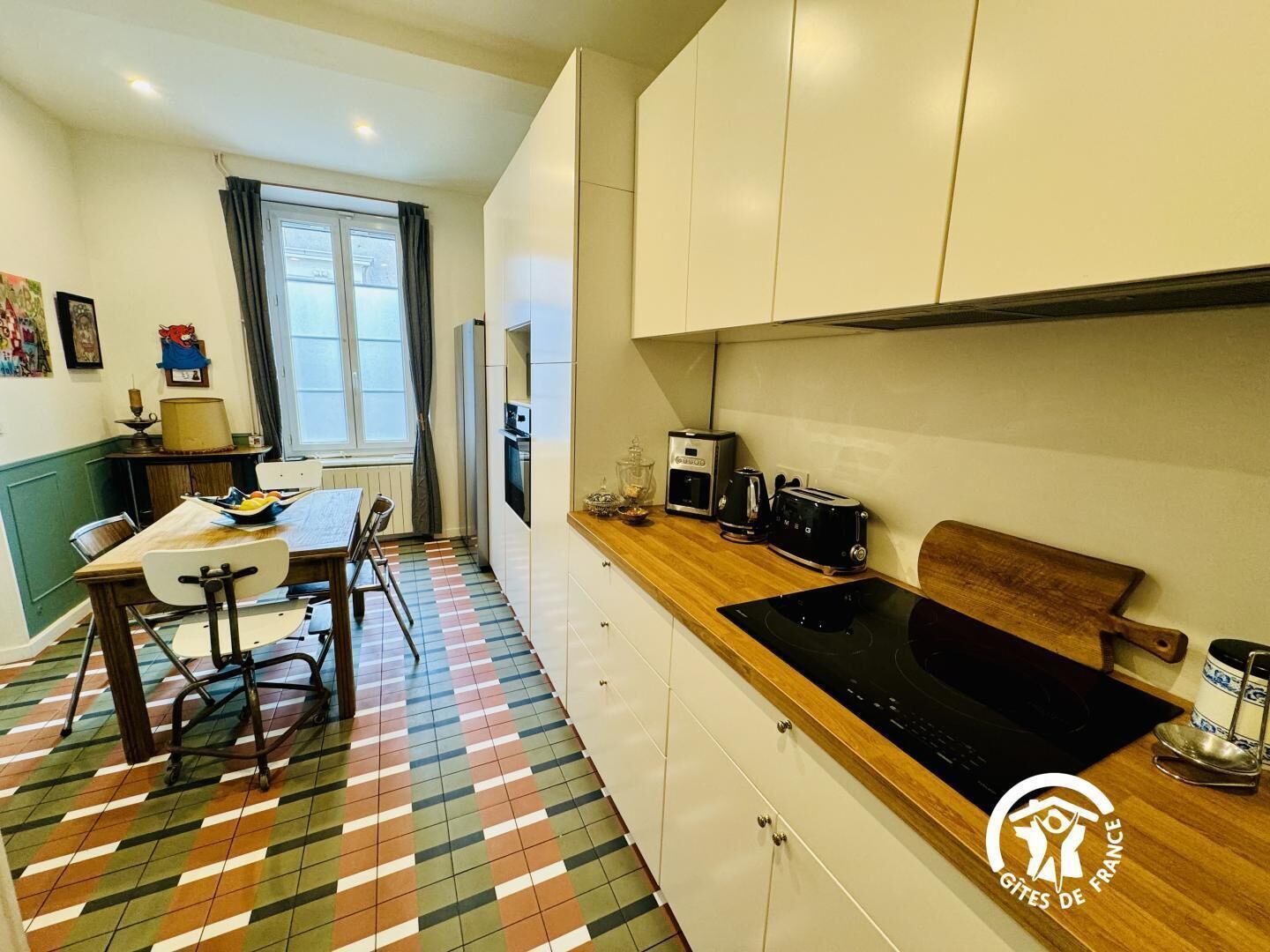 A compact kitchen with white cabinets, a wooden countertop, a black induction cooktop, and a window with curtains.