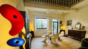 Un vaste salon doté d’un plancher en bois, un coin repas avec une table en verre et des chaises modernes, et un grand tableau abstrait accroché au mur.