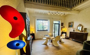 Un salón amplio con suelo de madera, una zona de comedor con mesa de vidrio y sillas modernas, y un cuadro abstracto grande en la pared.