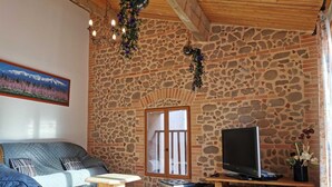 Een gezellige woonkamer met een stenen muur, een bank, een televisie en een bijzettafeltje.