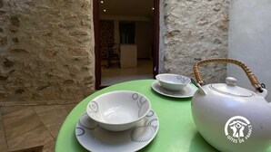 Un pequeño espacio al aire libre con pared de piedra, una mesa verde, tetera blanca y tazas a juego.