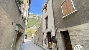 Una calle estrecha flanqueada por edificios, una tienda visible con un letrero y una montaña al fondo.