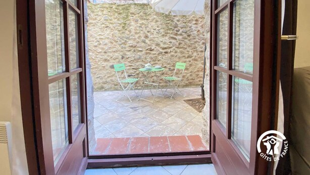 Puerta abierta que da a un patio con paredes de piedra, dos sillas verdes y una mesa.