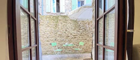 Un patio con paredes de piedra, una mesa y sillas, una sombrilla y vistas a un edificio con persianas.