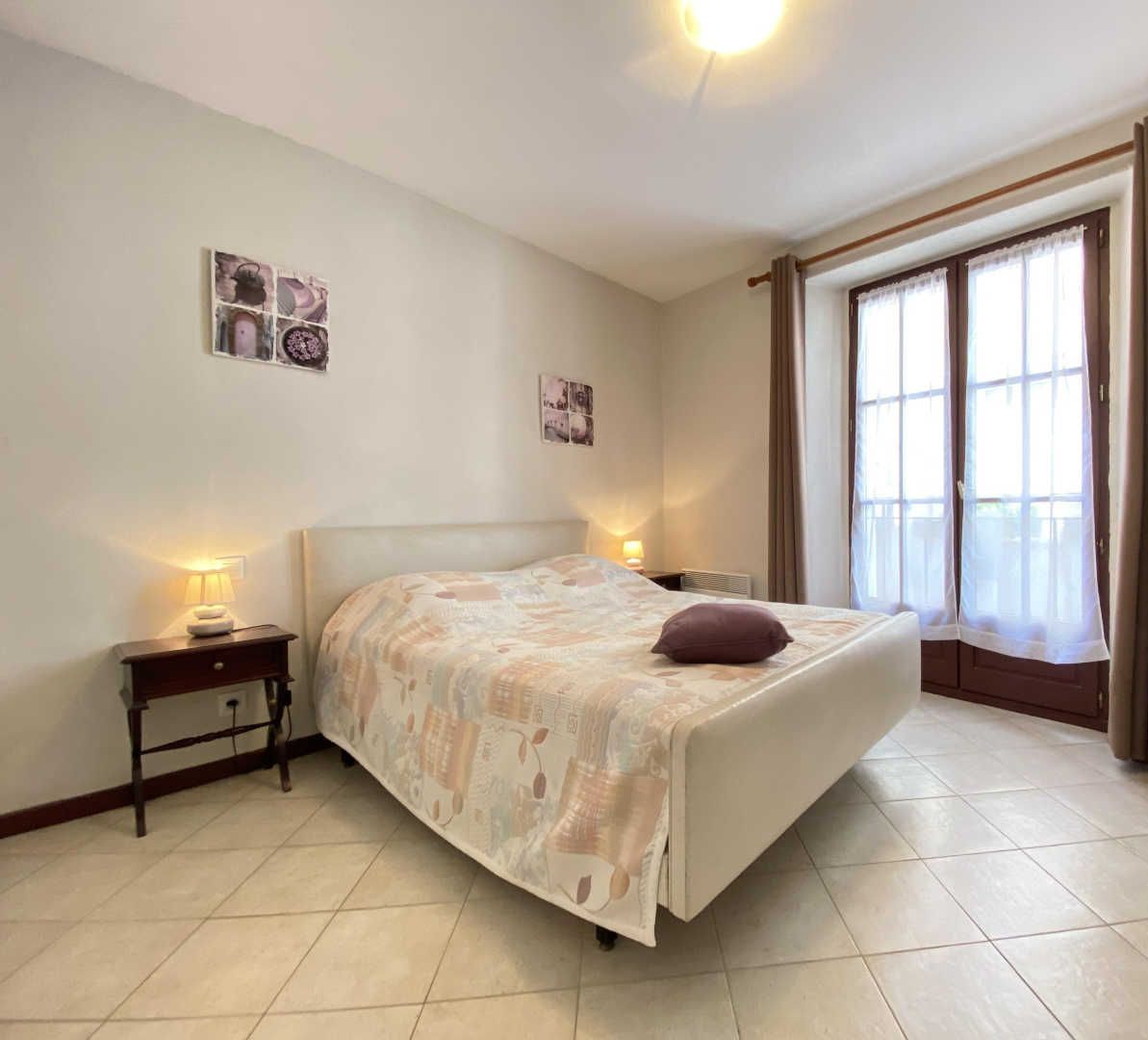 A bedroom with a bed, bedside tables, a chair, and a large window with curtains.