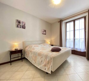 Une chambre à coucher avec un lit, des tables de chevet, une chaise et une grande fenêtre avec des rideaux.