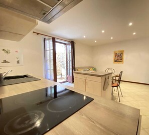 Une cuisine équipée d’une cuisinière, d’un évier et d’un coin repas. On y trouve une fenêtre avec des rideaux, un mur en pierre et une petite table avec des chaises.