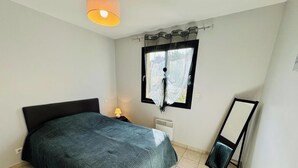 Un dormitorio con cama, mesita de noche, lámpara, ventana con cortinas y espejo.