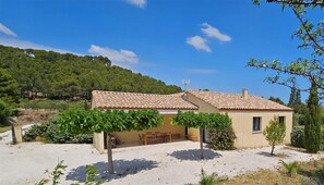 Une maison à deux étages avec un toit en tuiles, une terrasse avec une table et des chaises, et une allée gravillonnée.
