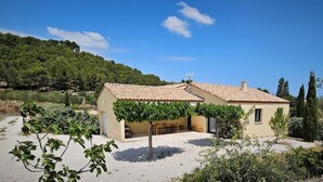Un edificio de dos pisos con techo de tejas, un patio cubierto con mobiliario exterior y vistas a un paisaje montañoso.