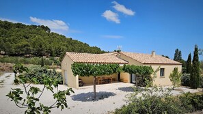 A two-story building with a tiled roof, a covered patio area with outdoor furniture, and a view of a hilly landscape.