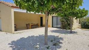 A building with a patio area, a table with chairs, and a tree in the foreground.