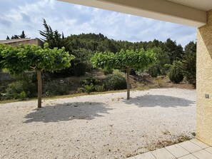 A gravel patio with a pergola and a view of a forested hillside.