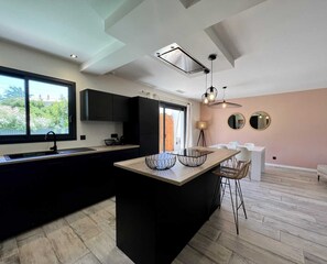 Una cocina moderna con una isla grande, armarios negros y vistas al exterior a través de un ventanal.