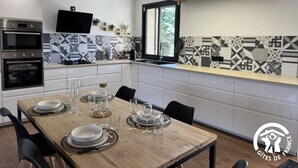 Une cuisine moderne dotée d’appareils électroménagers intégrés, une table à manger pour quatre personnes et une grande fenêtre laissant entrer la lumière naturelle.
