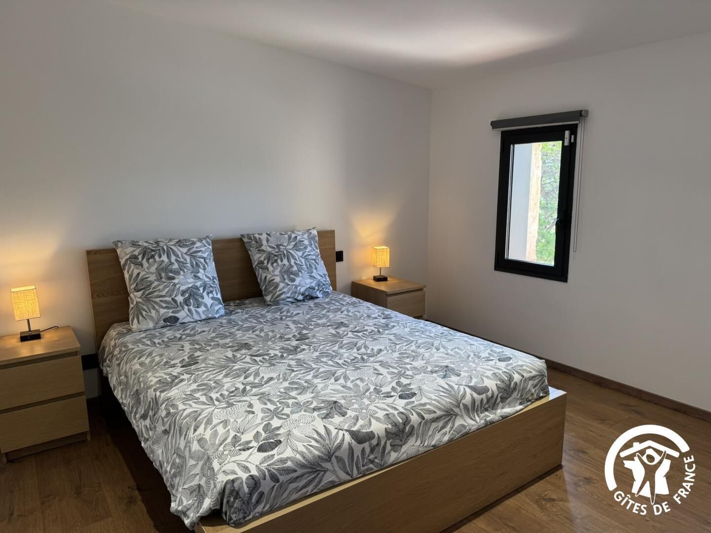 Een slaapkamer met een bed, twee nachtkastjes, een raam en een logo op de muur.
