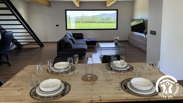 Un salon moderne avec un grand téléviseur, un canapé et une table à manger pour quatre personnes.