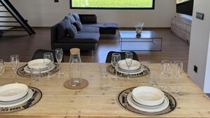 Un salon moderne avec une table à manger en bois, préparée pour accueillir six personnes, un canapé foncé et un grand écran de télévision diffusant un paysage pittoresque.