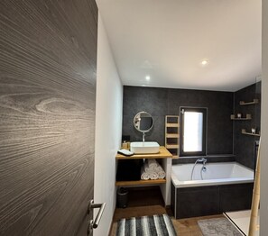 Un baño moderno con tocador de madera, un espejo redondo, una bañera y un ventanal.